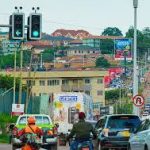 Urban street in Uganda with cars, motorcycles, and hillside buildings, showing daily transport and infrastructure.
