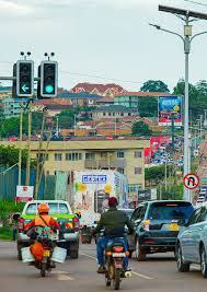Urban street in Uganda with cars, motorcycles, and hillside buildings, showing daily transport and infrastructure.